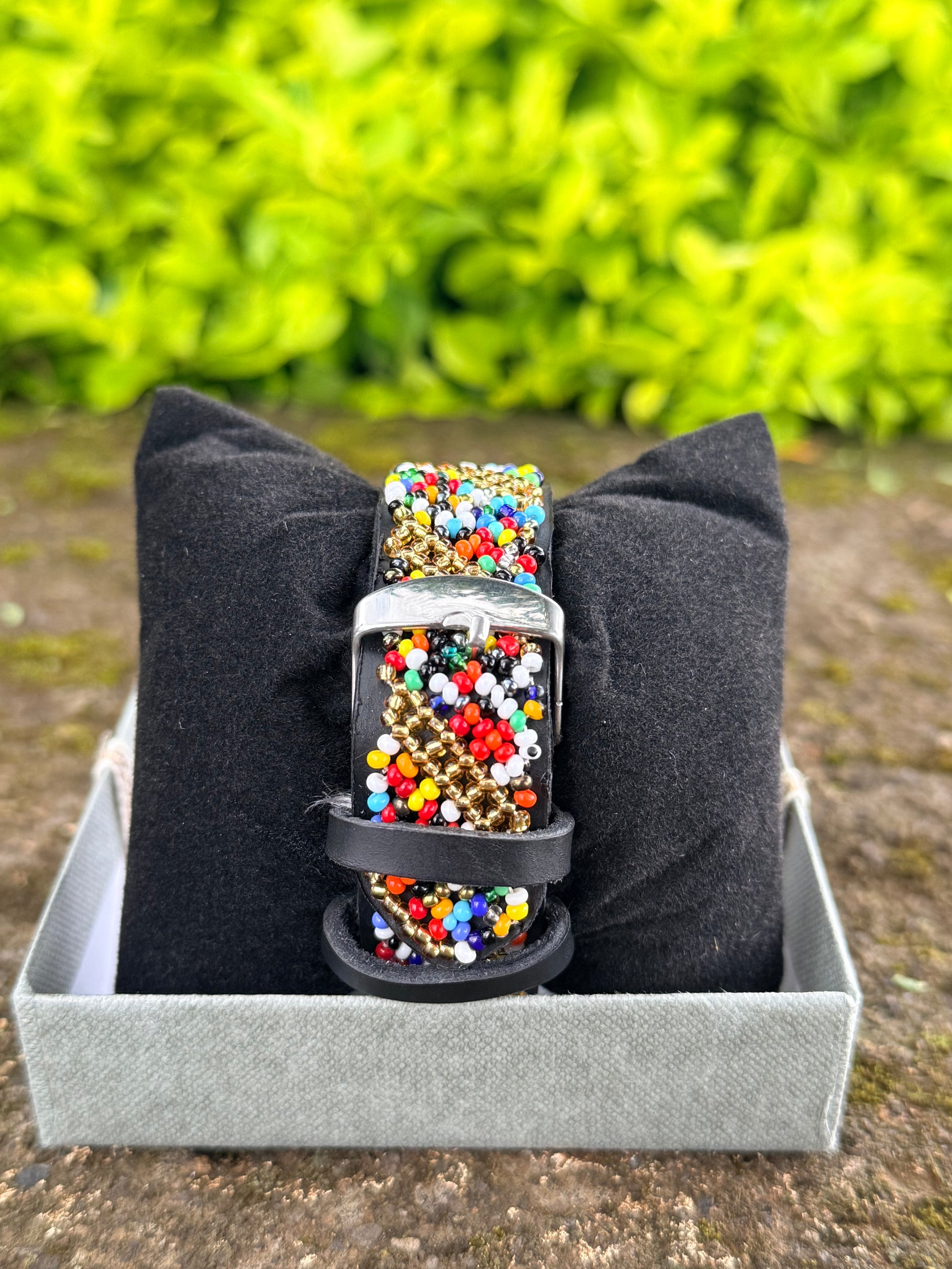 Colorful beaded belt on a black cushion with a blurred green background