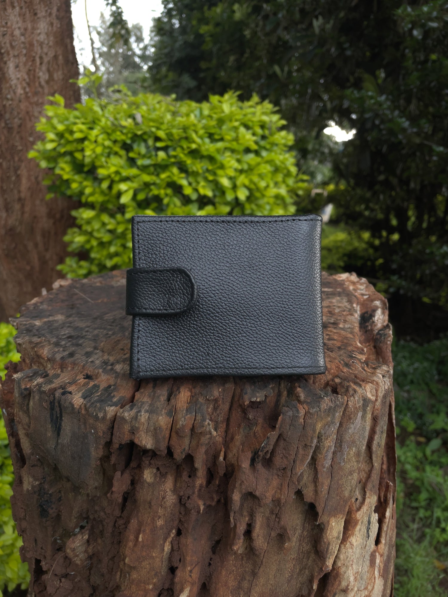 Black leather wallet on a wooden log with greenery in the background